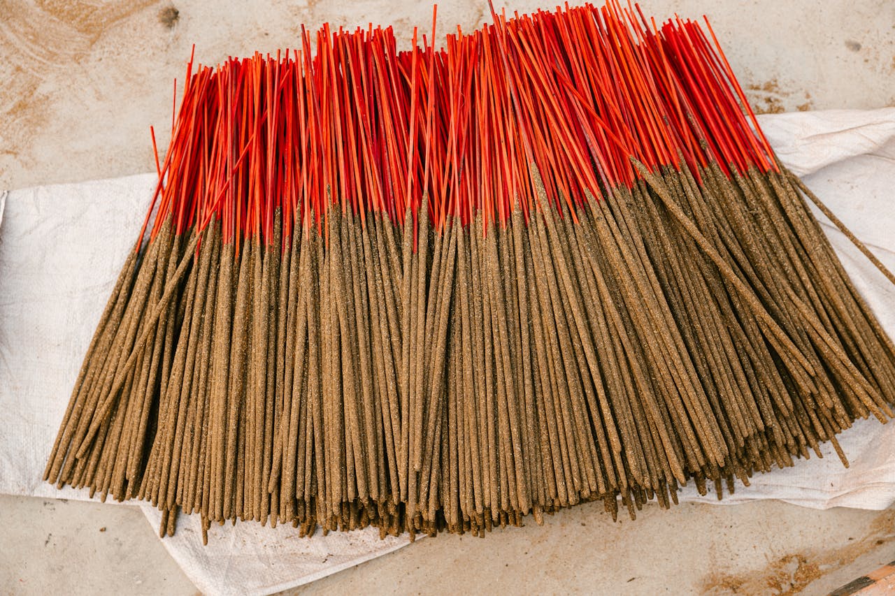 A collection of handcrafted incense sticks with vibrant red tips spread on white fabric, creating a striking visual.